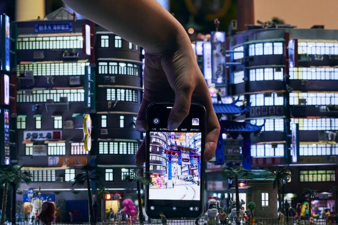 A modeler's hand above a glowing miniature city at Small Worlds Tokyo, the largest miniature museum in Tokyo