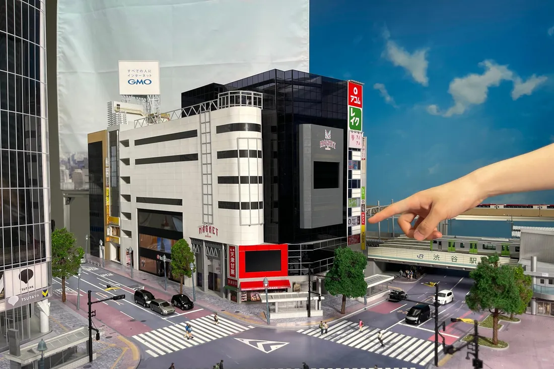 A miniature Shibuya crossing diorama with tiny pedestrians and glowing screens, part of the Small Worlds Tokyo tickets experience