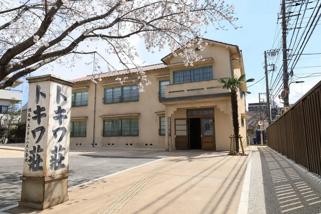 The rebuilt apartment block of the Tokiwa-so Manga Museum in Toshima, with a cherry tree and its wooden sign at the entrance